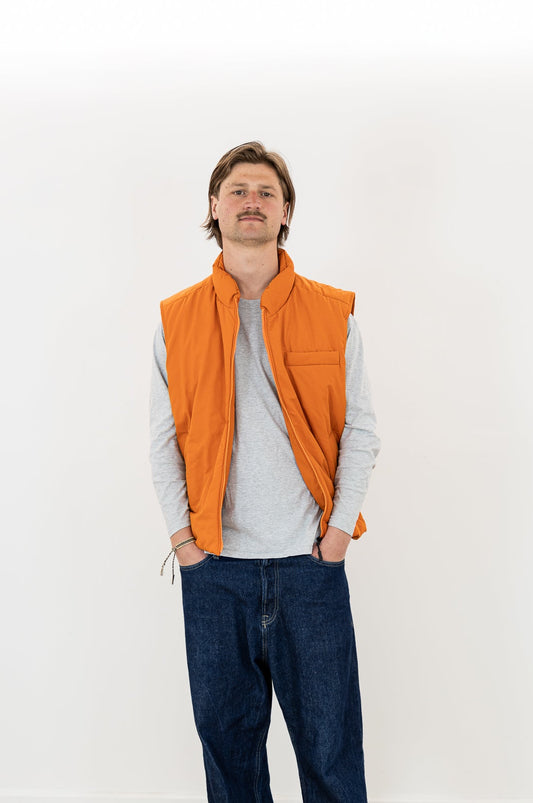 Man wearing an orange bodywarmer over a gray shirt on a white background